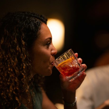 Woman with long curly brown hair sipping a cocktail