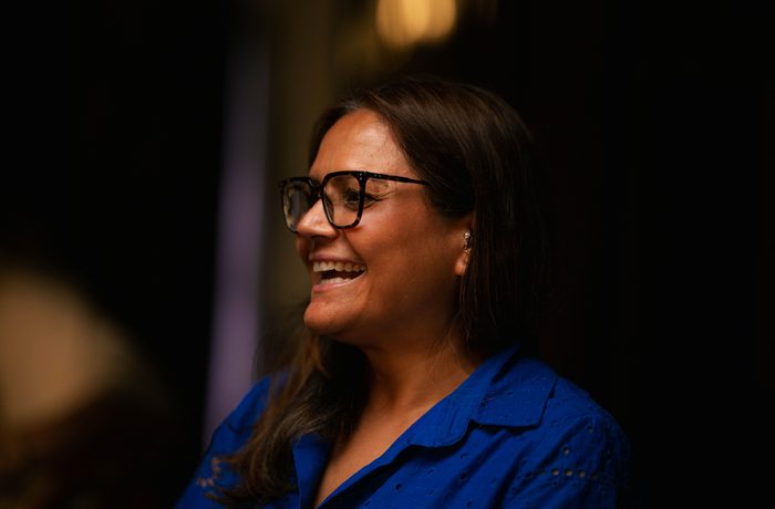 Woman with long hair, round glasses and a blue shirt smiling