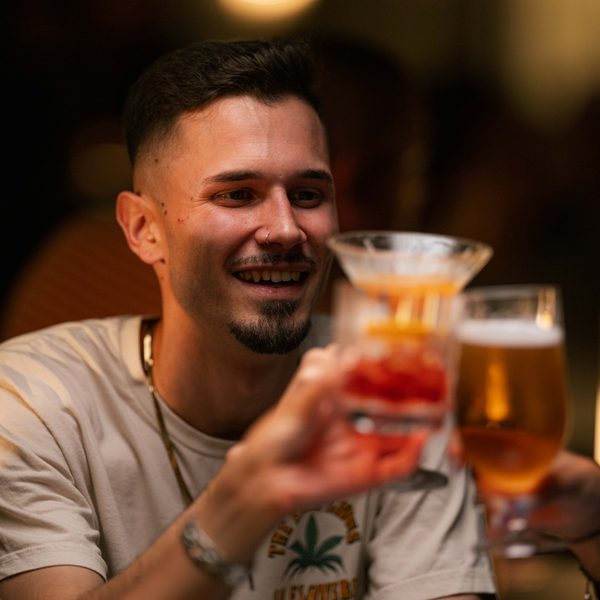 Man with short brown hair and goatee, saying cheers with his drink