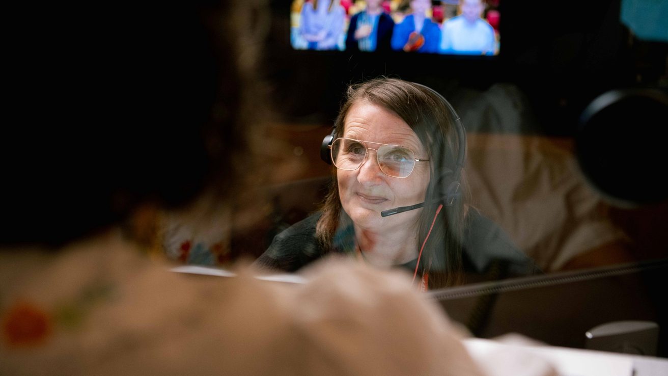 A white woman with short brown hair wearing an earpiece talking to a customer at Box Office