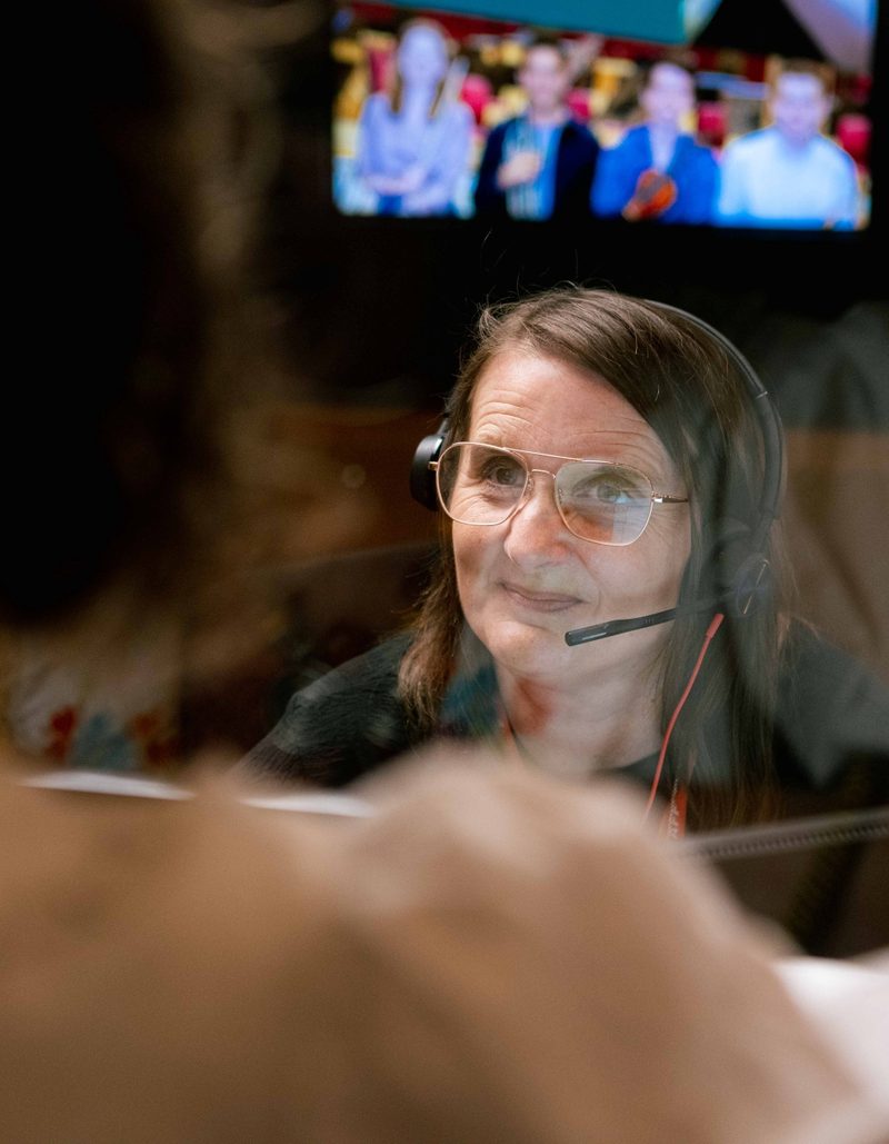 A white woman with short brown hair wearing an earpiece talking to a customer at Box Office