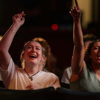 Two audience members singing along with their arms in the air