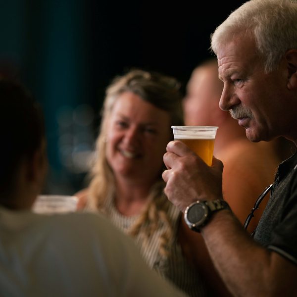 A white man with short grey hair and a moustache about to take a sip of his beer