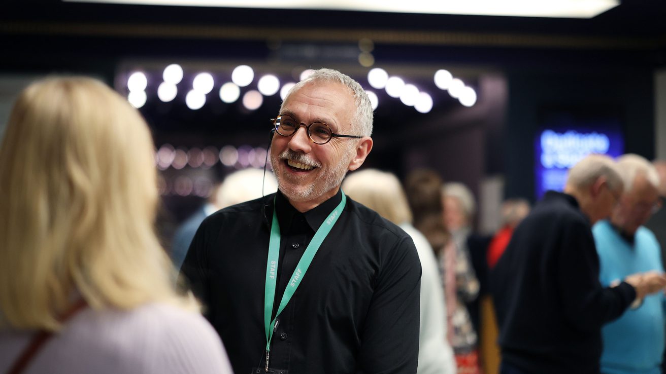 A male member of the Front of House team greeting an audience member in the foyer