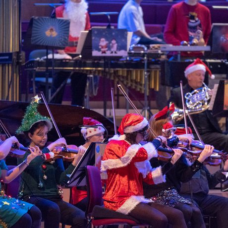 Members of the violin section dressed in Christmas outfits and playing their instruments