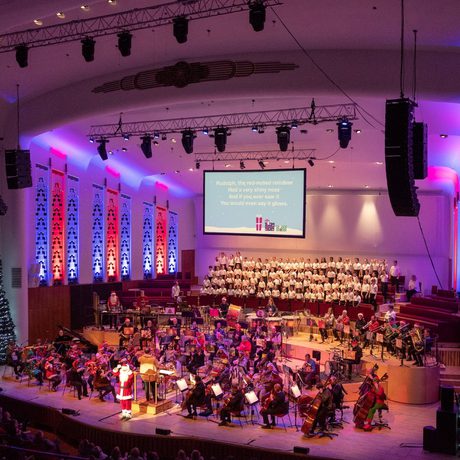 A wide shot of the Liverpool Philharmonic stage decorated with Christmas trees and rainbow lighting