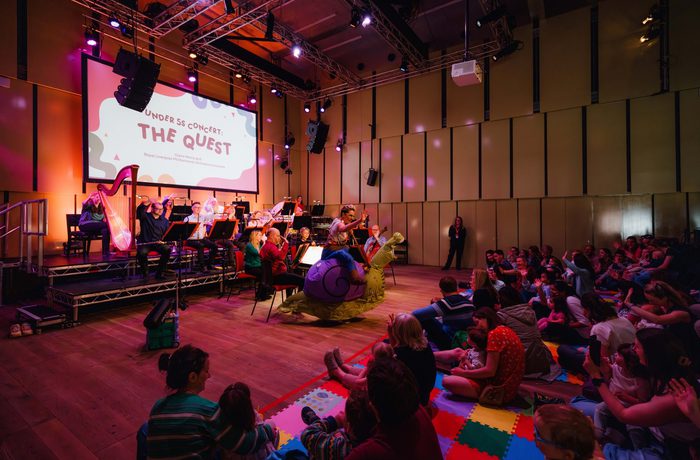Claire Henry, dressed as an inflatable snail, stood in front of an audience sat on the Music Room floor on colourful mats
