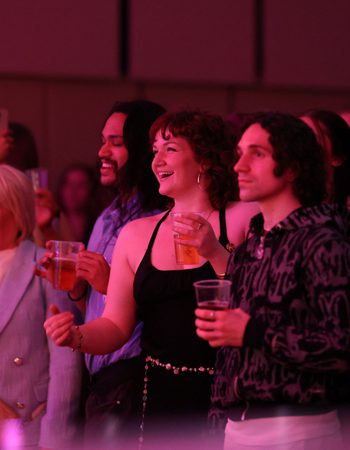 Two female and one male member of the audience standing and watching a concert in the Music Room