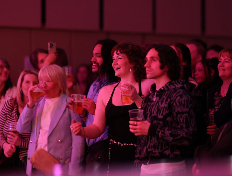 Two female and one male member of the audience standing and watching a concert in the Music Room