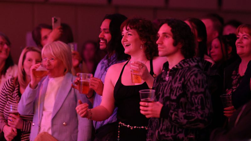 Two female and one male member of the audience standing and watching a concert in the Music Room
