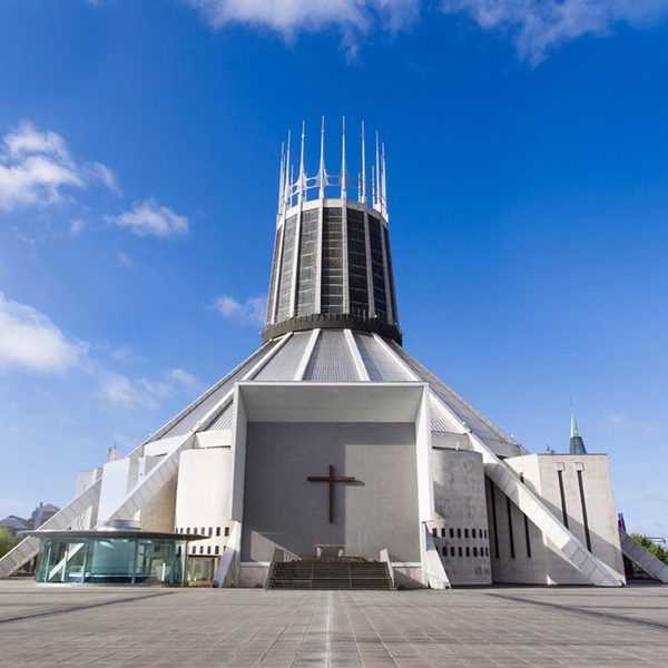 A white cathedral with a large cross displayed in the centre, with several spikes pointing upward on the roof in front of a blue sky