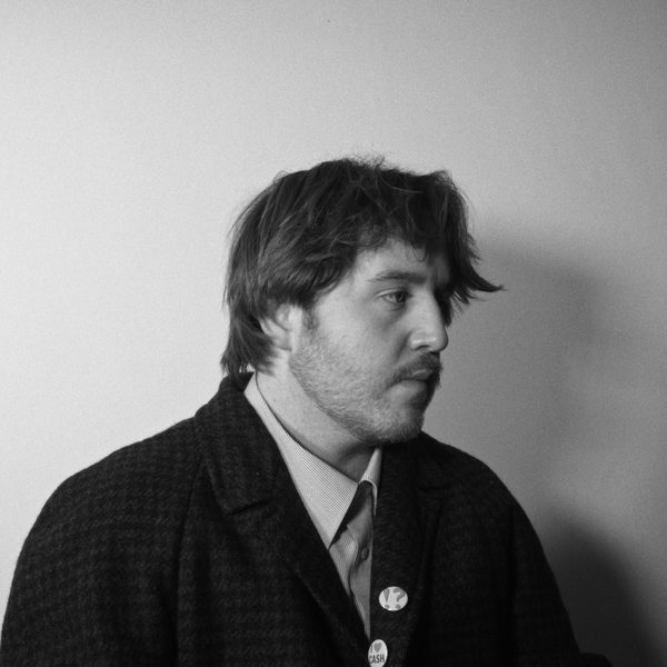 Young white man looking pensive in black blazer with badges