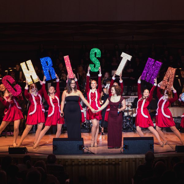 Dancers in red dresses holding up letters that spell Christmas