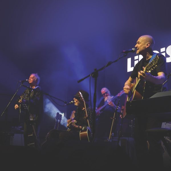 A four man band playing on a purple lit stage.