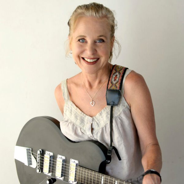 Kristin Hersh smiling at the camera with a grey guitar