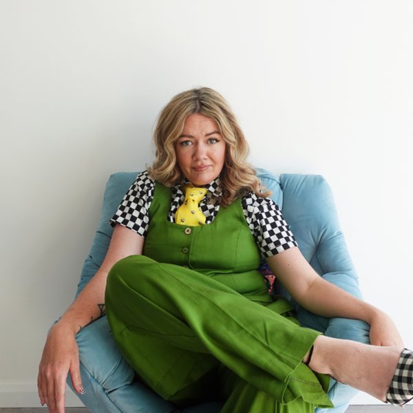 Serena Terry sitting on a blue chair wearing green overalls and looking into the camera