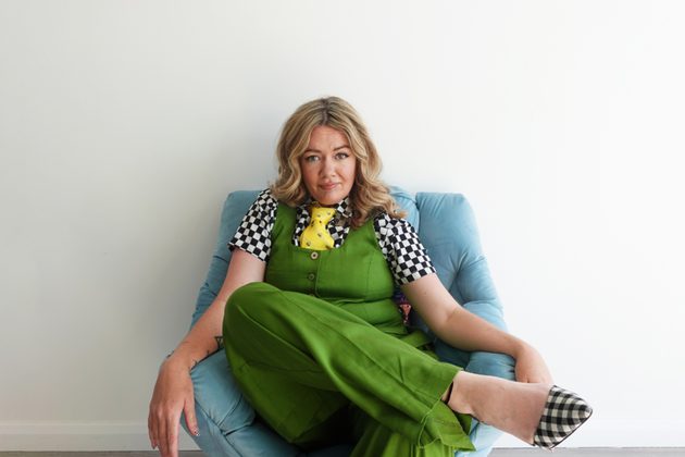 Serena Terry sitting on a blue chair wearing green overalls and looking into the camera