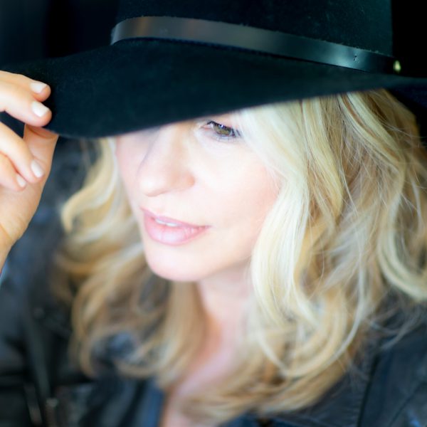 Vonda Shepard staring at the bottom left corner wearing and holding a black hat