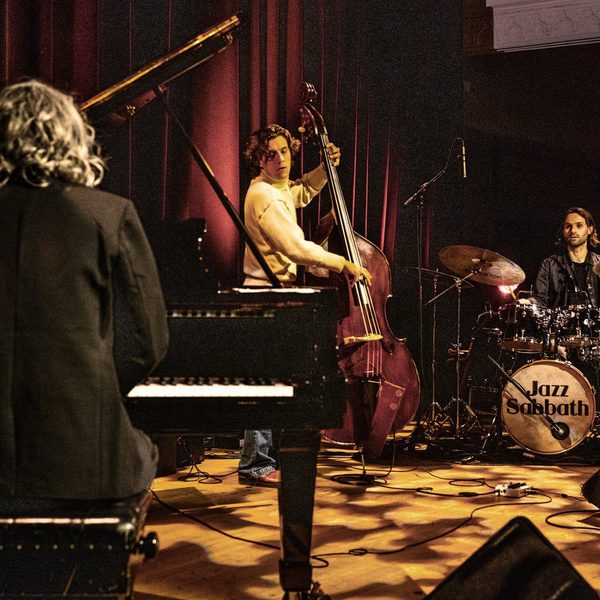 3 members of Jazz Sabbath performing in a studio surrounded by burgundy curtains