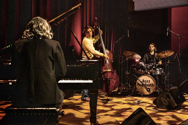 3 members of Jazz Sabbath performing in a studio surrounded by burgundy curtains