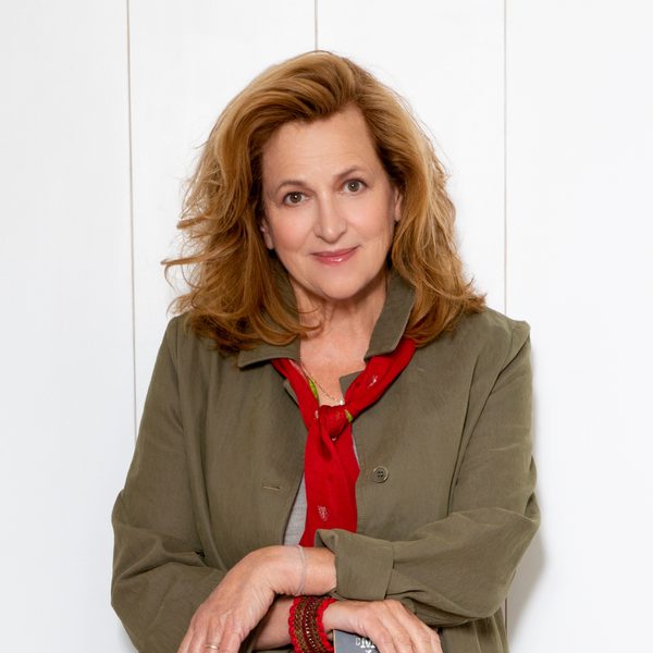 Barbara Dickson, a white woman with brown wavy hair smiling at the camera, wearing a dark grey blazer and a thin red scarf