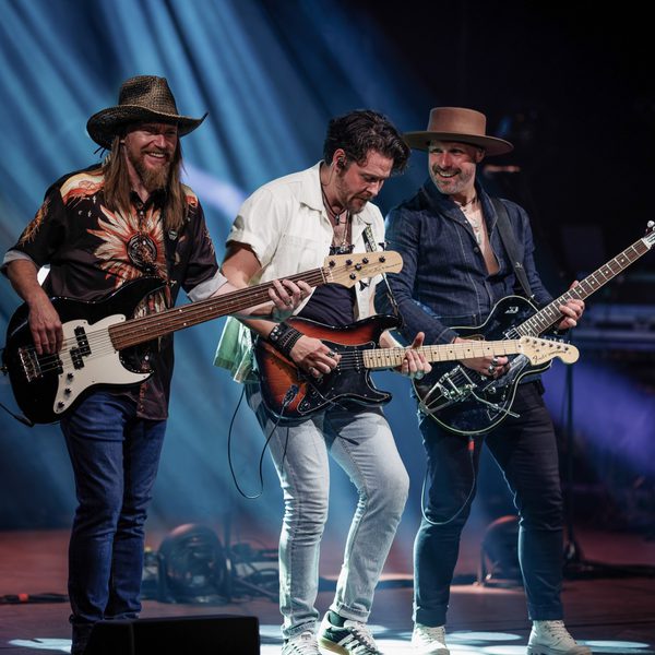 Three members of The Illegal Eagles performing on stage with electric guitars