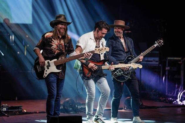 Three members of The Illegal Eagles performing on stage with electric guitars