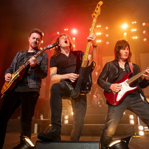 Three members of the The Classic Rock Show performing in stage with guitars