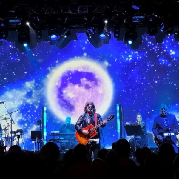 Members of The ELO Show performing onstage, against a night scene backdrop