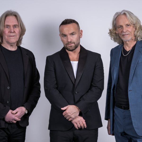Members of Wet Wet Wet stood in a row looking at the camera with serious expressions in front of a white background