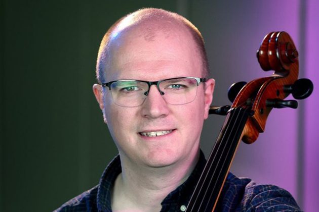 Mark Lindley, a white bald man with round glasses, holding his cello
