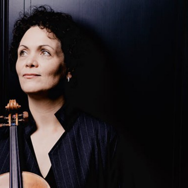 Tabea Zimmerman, a white woman with black curly hair, holding her viola and looking over to the left