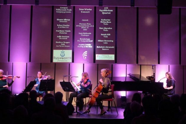 Members of a string quartet performing on stage surrounding by purple lighting