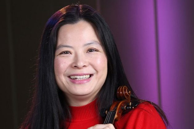 Qian Wu, an Asian woman with long black hair, wearing a red jumper and holding her violin