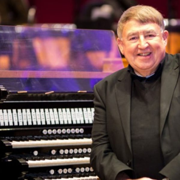 Ian Tracey, a white man with short grey hair, wearing a black suit sat next to an organ