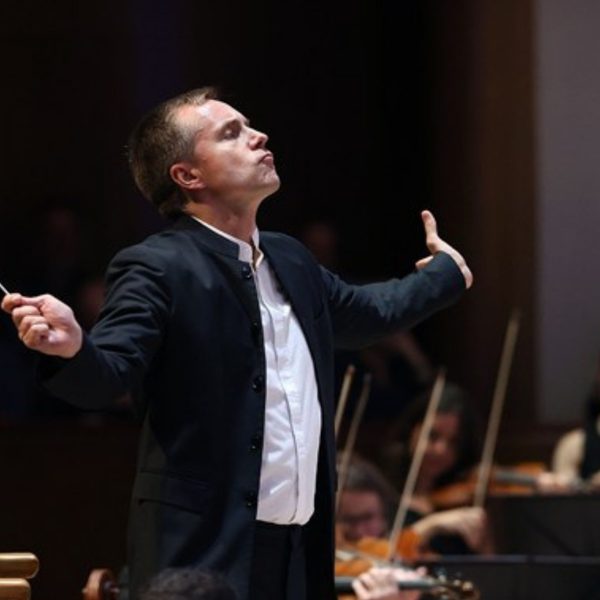 Vasily Petrenko, a tall white man with short brown hair, wearing a black suit conducting the orchestra with his arms outstretched
