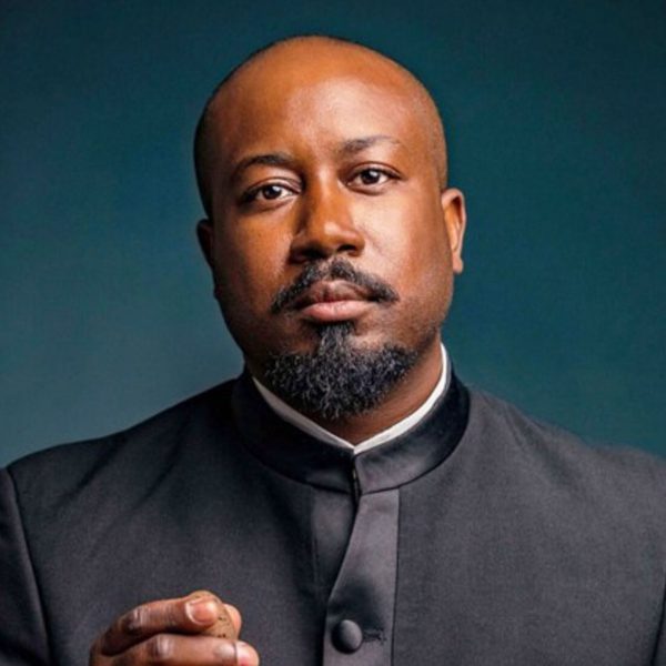 Kellen Grey, a bald black man with a goatee, wearing a black suit looking directly at the camera