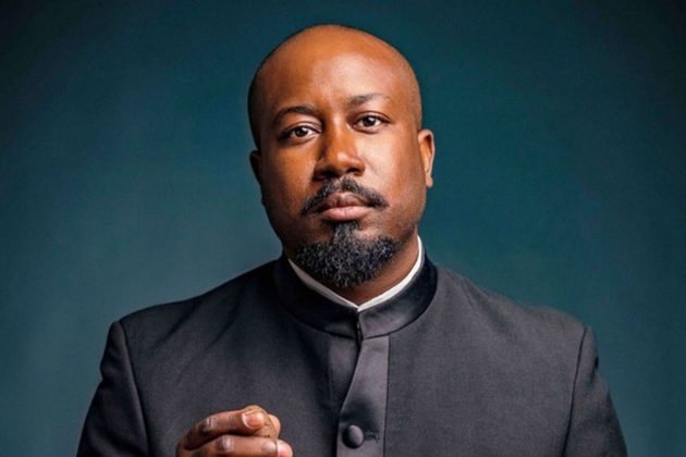 Kellen Grey, a bald black man with a goatee, wearing a black suit looking directly at the camera