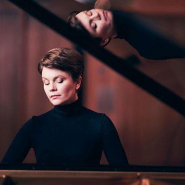 Clare Hammond, a white woman with short brown hair, sat at an open piano wearing a black turtleneck