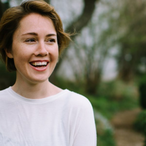 Caroline Shaw, a white woman with short brown hair, wearing a white top and smiling to the right in a garden