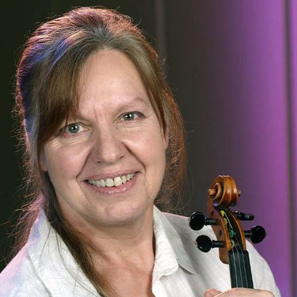 Thelma Handy, a white woman with long brown hair, wearing a white shirt and holding her violin