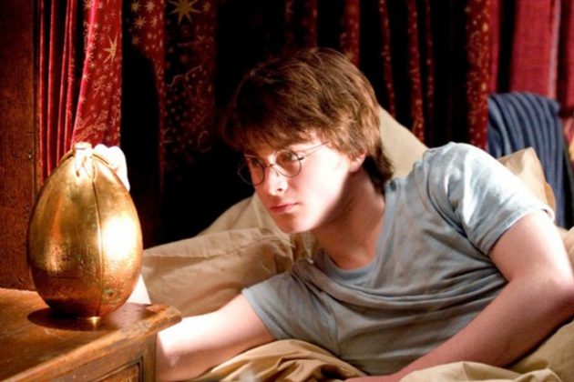 Harry Potter, a white boy with short brown hair and round glasses, lying in bed touching a golden egg