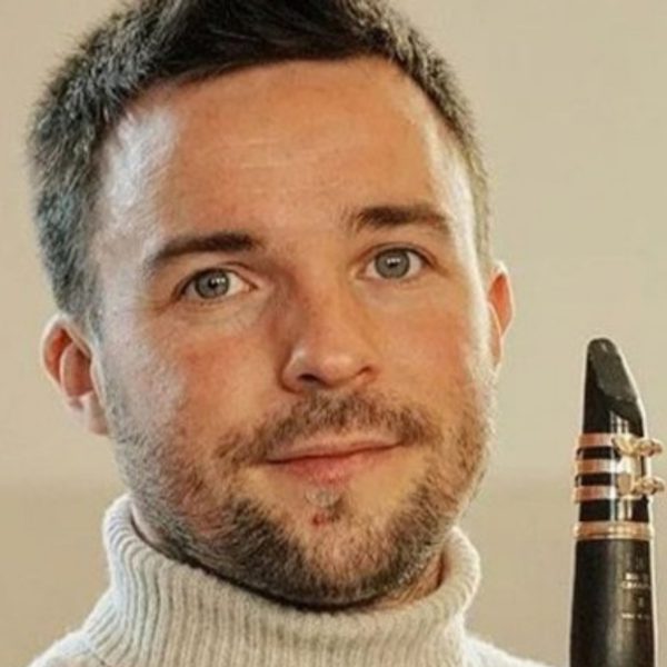 Miquel Ramos Salvadó, a white man with short brown hair and a beard, wearing a white turtleneck and holding his clarinet