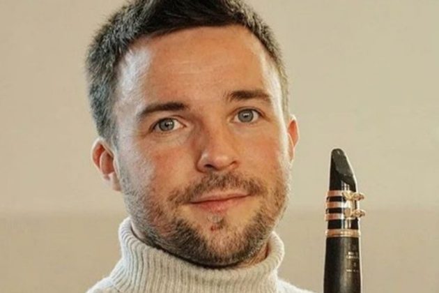 Miquel Ramos Salvadó, a white man with short brown hair and a beard, wearing a white turtleneck and holding his clarinet