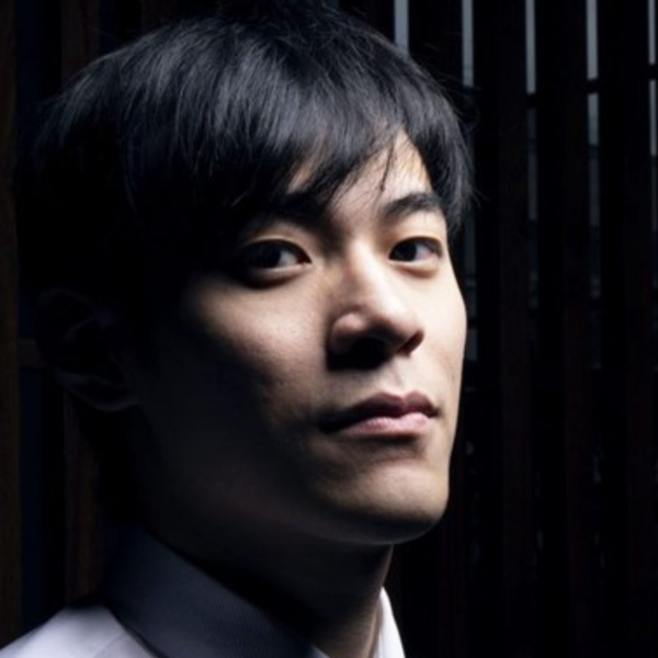 Kai-Min Chang, an Asian man with short black hair, looking directly at the camera in a dark room