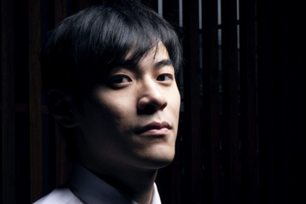 Kai-Min Chang, an Asian man with short black hair, looking directly at the camera in a dark room