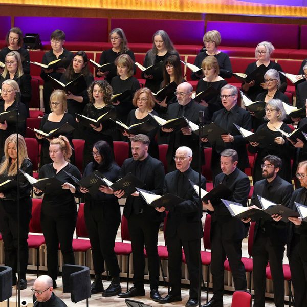 Members of the Choir dressed in all black singing on stage holding music folders