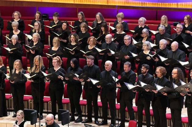Members of the Choir dressed in all black singing on stage holding music folders