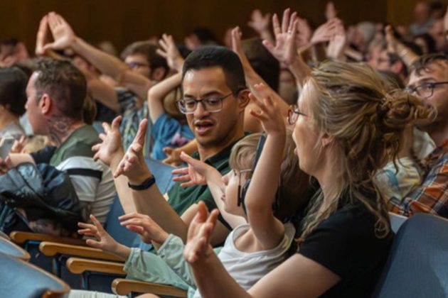 A mother, father and young child sat in an auditorium with their arms in the air
