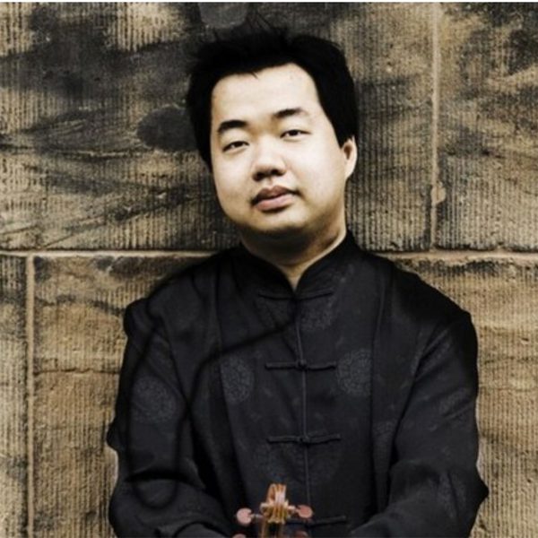 Ning Feng, an Asian man with short black hair, wearing a black tunic and leaning against a stone wall